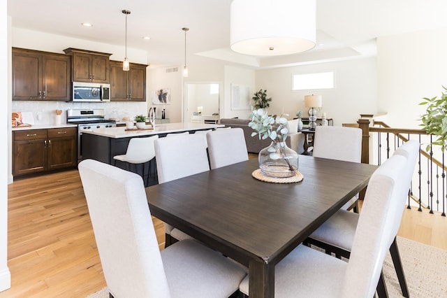 dining space with light wood-style flooring, recessed lighting, and a tray ceiling
