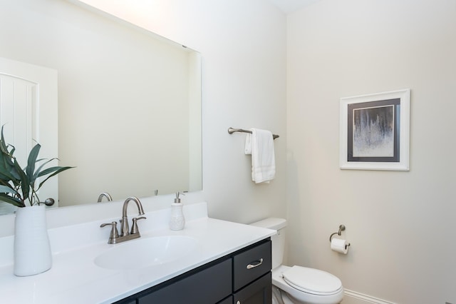 half bathroom with vanity, toilet, and baseboards