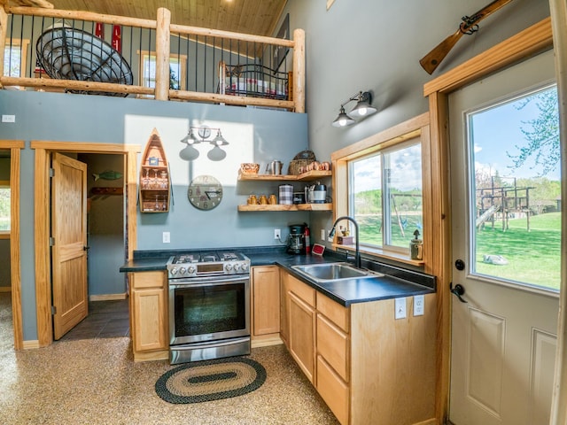 kitchen featuring stainless steel gas range oven, a sink, a high ceiling, dark countertops, and open shelves