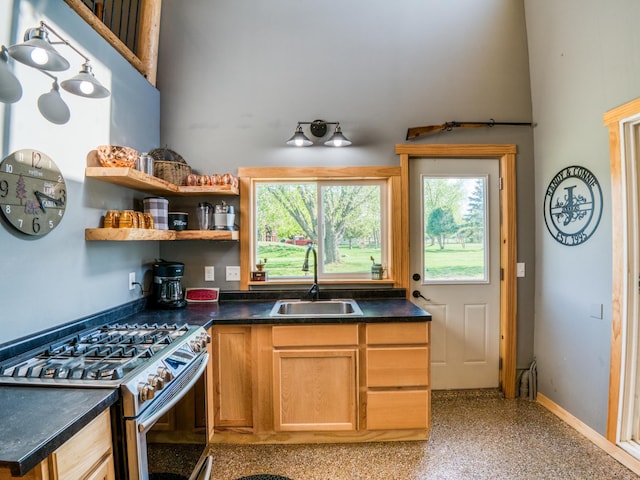 kitchen featuring stainless steel gas range, a sink, dark countertops, and baseboards