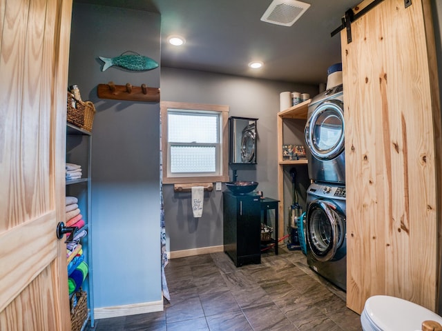 laundry room with estacked washer and dryer, a barn door, baseboards, and recessed lighting