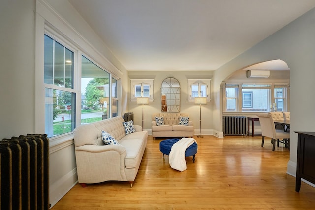 4448 Aldrich Ave S, Minneapolis, MN 55419 - living room featuring radiator heating unit, a wall mounted air conditioner, arched walkways, and light wood-style flooring