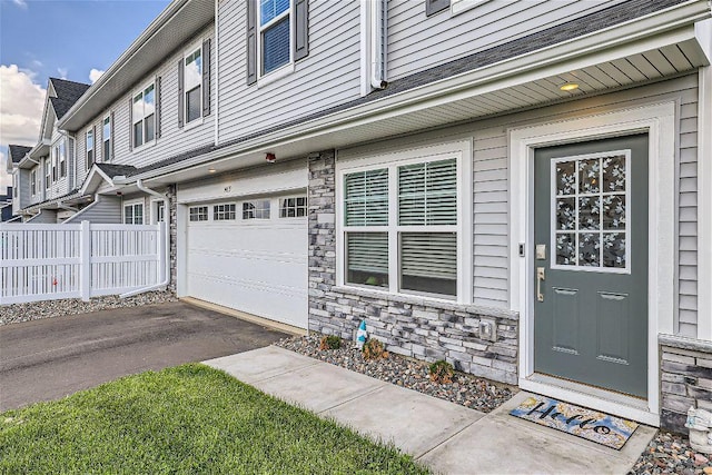 entrance to property with an attached garage, stone siding, fence, and driveway