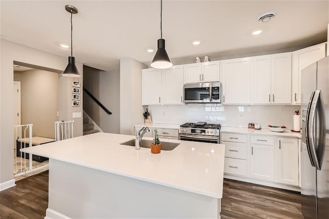 kitchen with appliances with stainless steel finishes, a sink, dark wood-style floors, white cabinetry, and tasteful backsplash