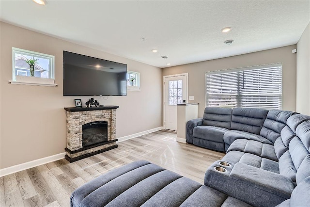 living room featuring light wood-style floors, baseboards, recessed lighting, and a stone fireplace