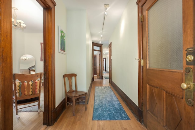 hall with light wood-style flooring, a chandelier, and baseboards