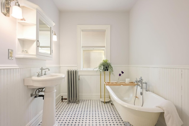 bathroom featuring radiator heating unit, a wainscoted wall, a freestanding bath, plenty of natural light, and a sink