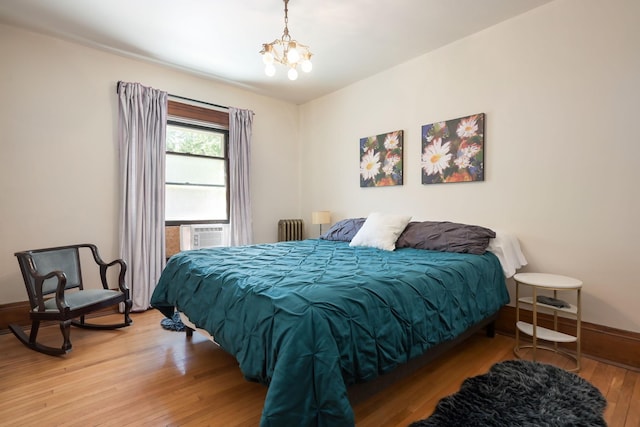 bedroom featuring radiator heating unit, light wood-style floors, a chandelier, baseboards, and cooling unit