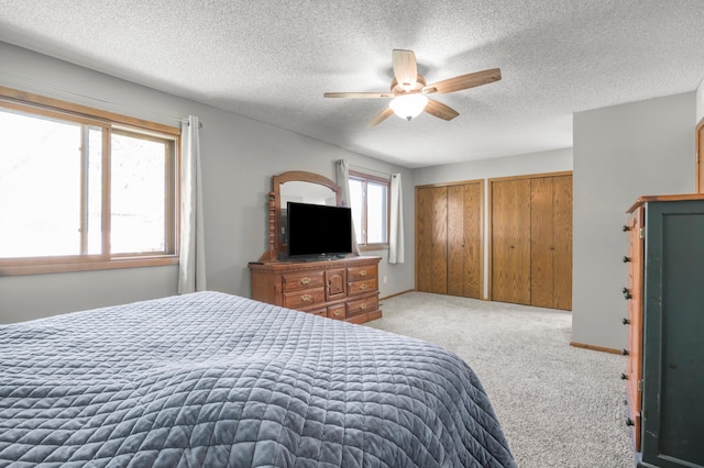 bedroom featuring two closets, light colored carpet, a textured ceiling, a ceiling fan, and baseboards