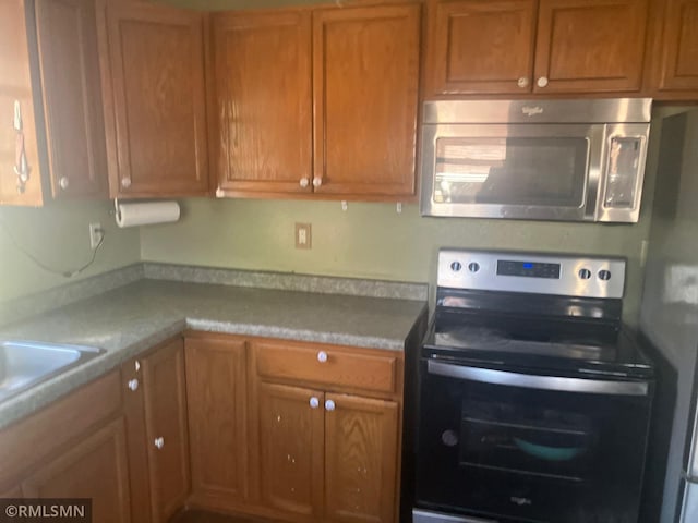 kitchen featuring stainless steel appliances, light countertops, a sink, and brown cabinetry