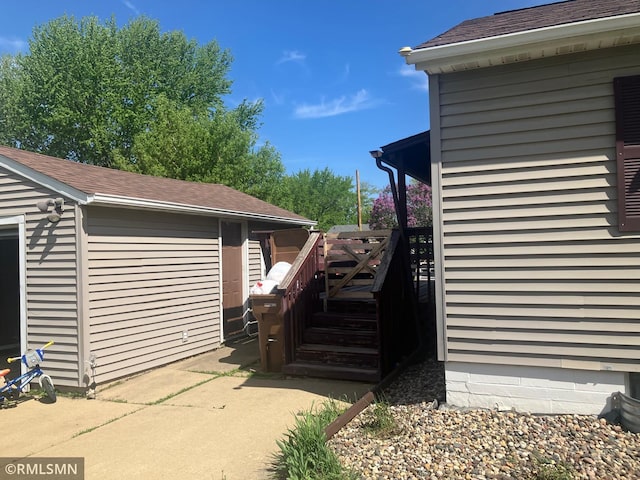 view of side of property featuring a wooden deck, roof with shingles, and a patio area