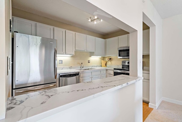 kitchen with appliances with stainless steel finishes, a sink, light stone countertops, baseboards, and white cabinetry