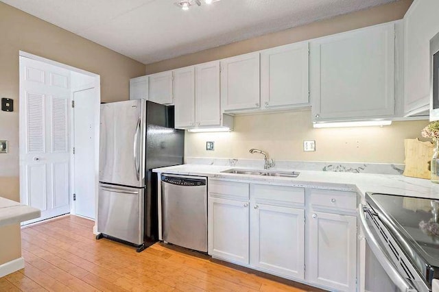 kitchen with appliances with stainless steel finishes, a sink, white cabinets, light countertops, and light wood finished floors