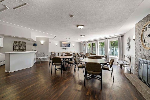 dining space with a textured ceiling, a brick fireplace, and dark wood-type flooring