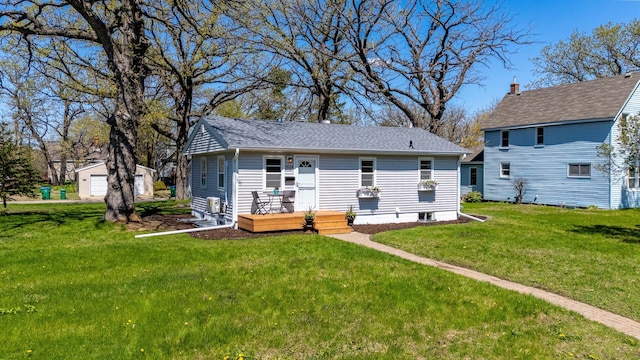 rear view of house featuring a yard, an outdoor structure, and a shingled roof