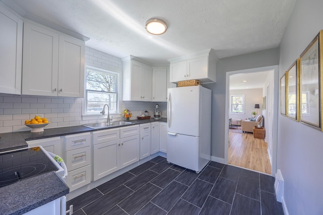 kitchen with freestanding refrigerator, a sink, white cabinetry, decorative backsplash, and dark countertops
