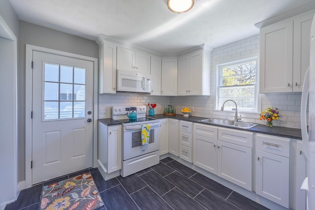 kitchen with white appliances, a sink, dark countertops, and white cabinets