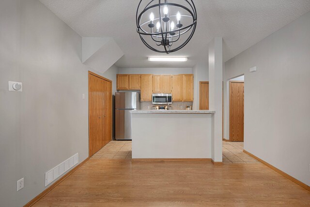 8497 Cortland Rd, Eden Prairie, MN 55344 - kitchen with appliances with stainless steel finishes, a chandelier, light countertops, light wood-style floors, and a textured ceiling
