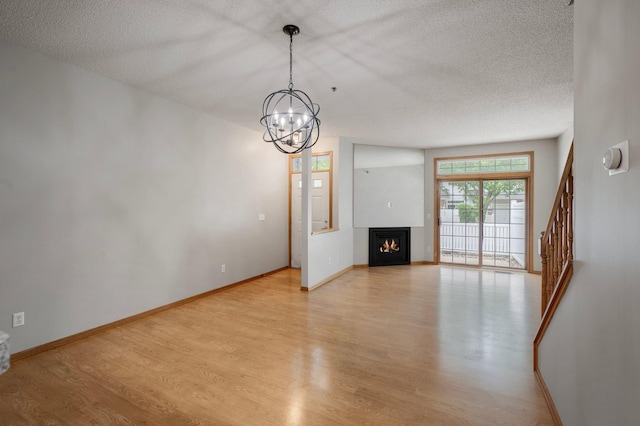 8497 Cortland Rd, Eden Prairie, MN 55344 - unfurnished living room with a textured ceiling, a chandelier, light wood-style floors, baseboards, and a lit fireplace