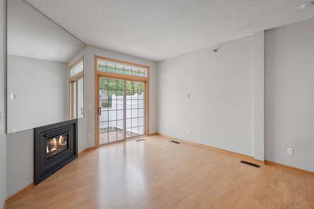8497 Cortland Rd, Eden Prairie, MN 55344 - unfurnished living room featuring wood finished floors, a textured ceiling, a glass covered fireplace, and baseboards