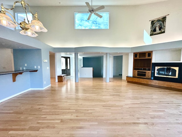 1976 Bay St, Worthington, MN 56187 - unfurnished living room featuring a towering ceiling, wood finished floors, a ceiling fan, baseboards, and a glass covered fireplace