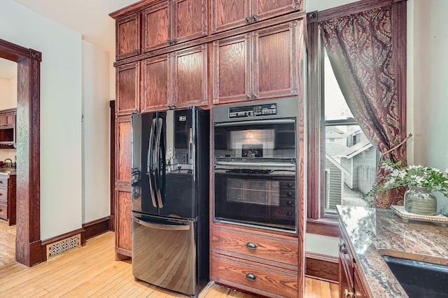 kitchen with black appliances, light wood-style floors, stone countertops, baseboards, and a sink