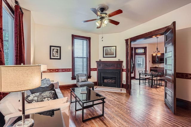 living area featuring a ceiling fan, wood finished floors, a glass covered fireplace, and baseboards