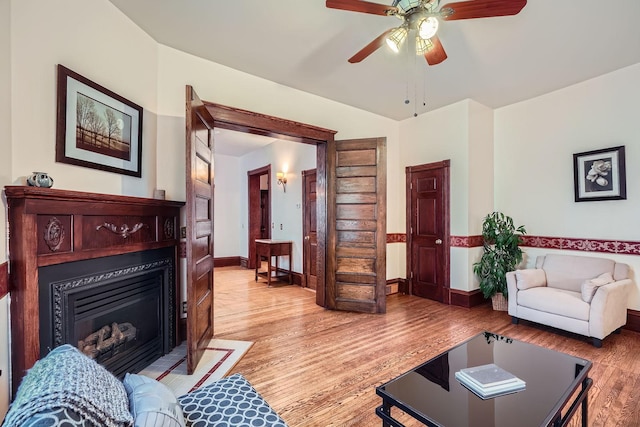 living area featuring a glass covered fireplace, light wood-style flooring, ceiling fan, and baseboards