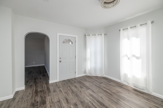 spare room featuring arched walkways, wood finished floors, baseboards, and plenty of natural light
