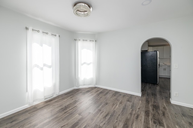 unfurnished room with dark wood-style floors, arched walkways, and baseboards