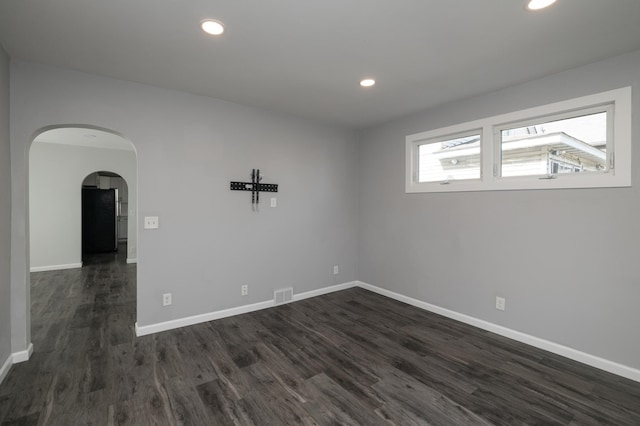 unfurnished room featuring dark wood finished floors, baseboards, arched walkways, and recessed lighting