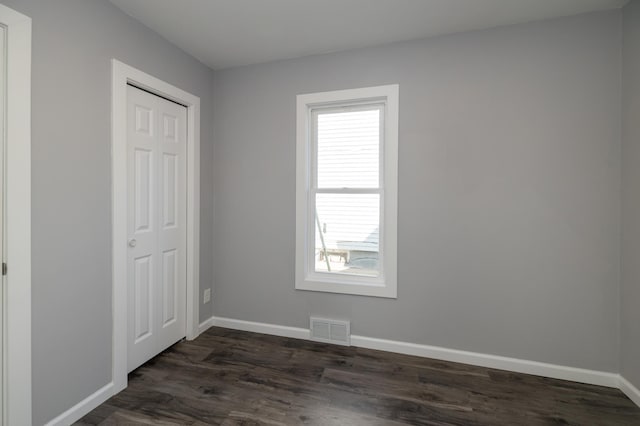unfurnished bedroom featuring multiple windows, dark wood-style floors, and baseboards
