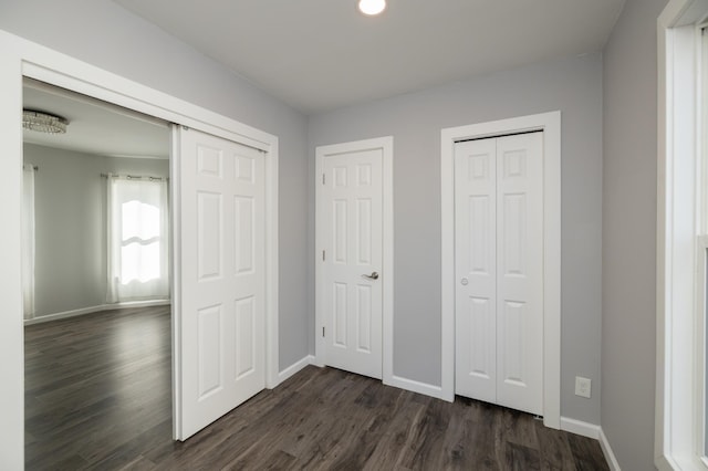 unfurnished bedroom with dark wood-type flooring, baseboards, and two closets