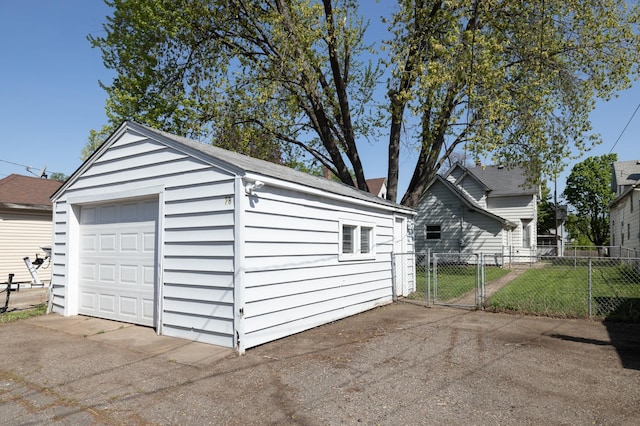 detached garage with fence, concrete driveway, and a gate