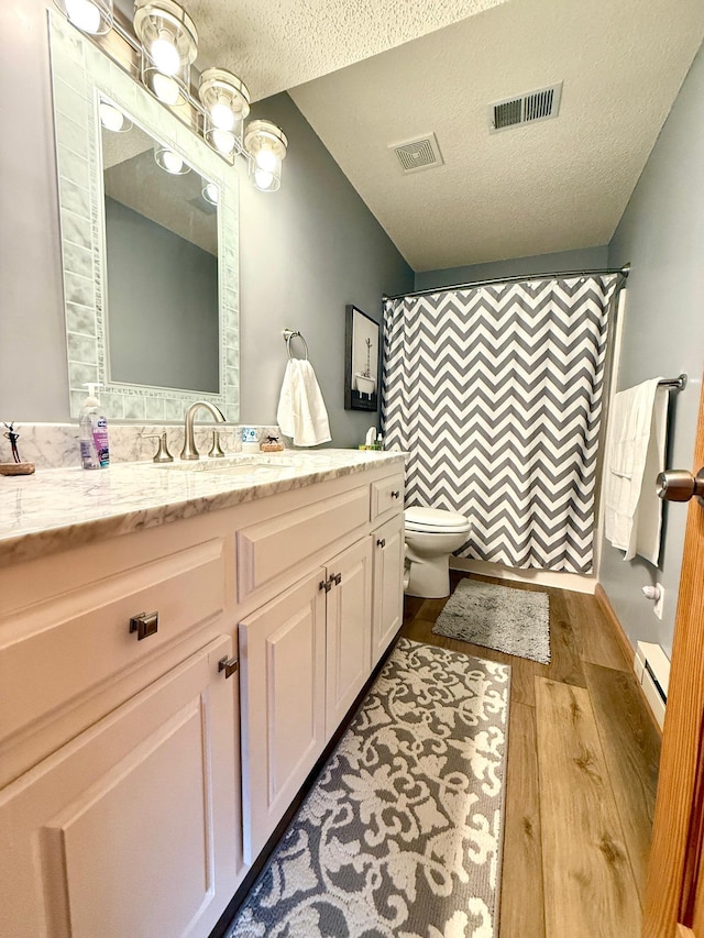 bathroom with baseboard heating, wood finished floors, a textured ceiling, toilet, and vanity