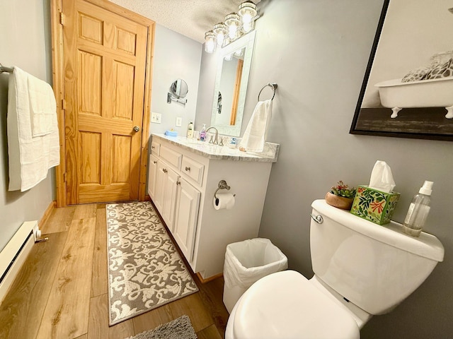bathroom with wood finished floors, vanity, toilet, and a baseboard heating unit