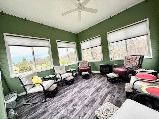 sunroom / solarium featuring track lighting, wood finished floors, baseboards, and a wood stove