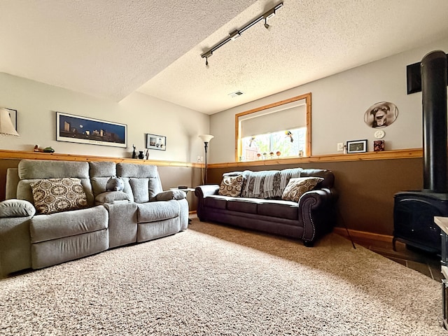 carpeted living room featuring a wood stove, a textured ceiling, baseboards, and track lighting