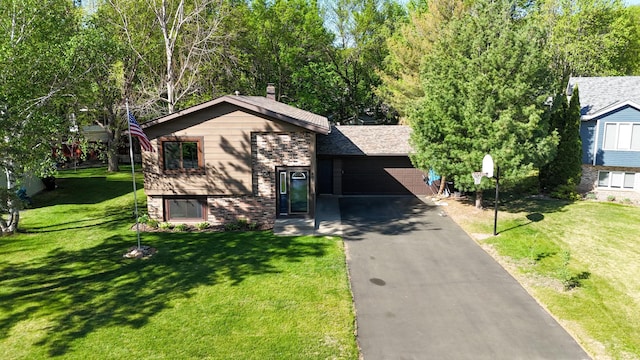 tri-level home featuring asphalt driveway, a front yard, brick siding, and a garage