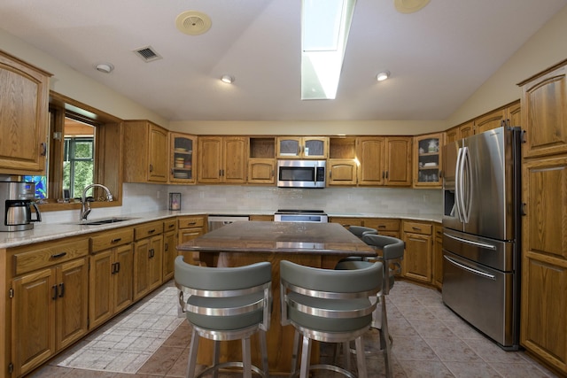 514 10th St N, Sartell, MN 56377 - kitchen featuring stainless steel appliances, a sink, brown cabinetry, backsplash, and vaulted ceiling