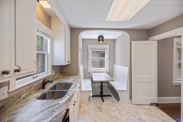 4505 47th Ave S, Minneapolis, MN 55406 - kitchen featuring a sink, white cabinetry, a drop ceiling, arched walkways, and baseboards