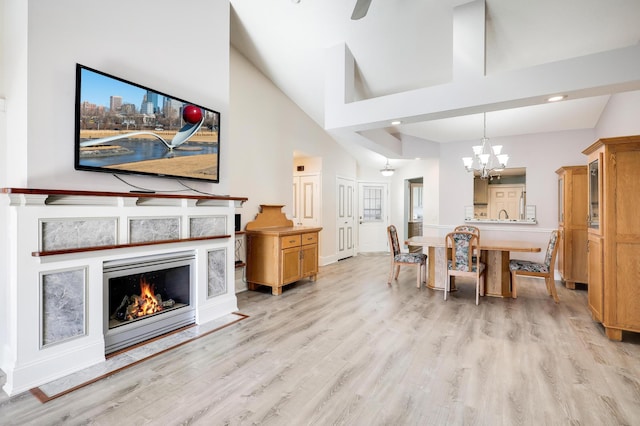 dining area with light wood-type flooring, a chandelier, a lit fireplace, recessed lighting, and high vaulted ceiling