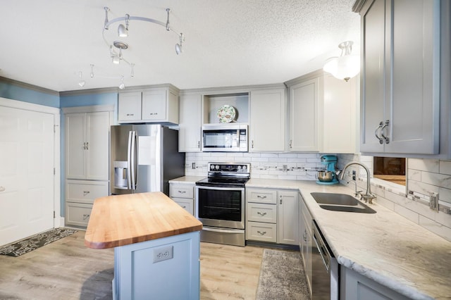 kitchen featuring appliances with stainless steel finishes, a sink, butcher block countertops, light wood-type flooring, and gray cabinetry