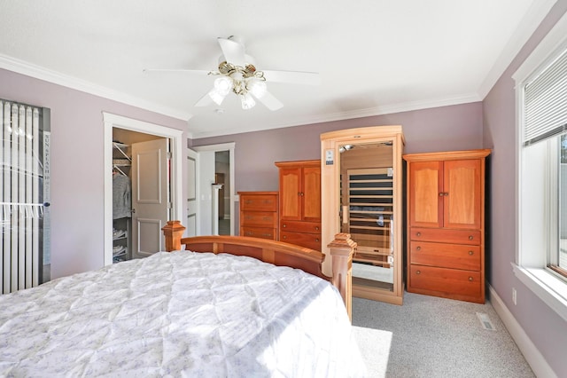 bedroom featuring light colored carpet, crown molding, a ceiling fan, baseboards, and a walk in closet