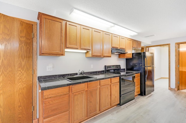 kitchen with black appliances, under cabinet range hood, a sink, light wood-style flooring, and a textured ceiling