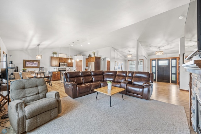 living room featuring light wood-style flooring, vaulted ceiling, and a stone fireplace