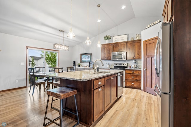 kitchen with stainless steel appliances, a sink, light wood finished floors, a kitchen breakfast bar, and high vaulted ceiling