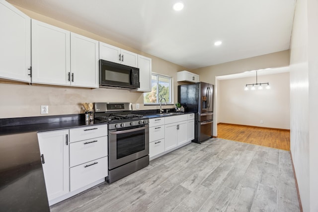 kitchen with stainless steel appliances, dark countertops, white cabinetry, a sink, and light wood finished floors