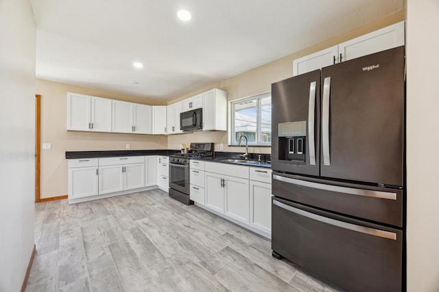 kitchen with stainless steel appliances, a sink, dark countertops, white cabinetry, and light wood-style floors