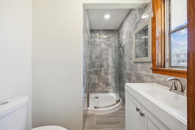 full bath featuring toilet, a stall shower, vanity, tile walls, and wood finished floors